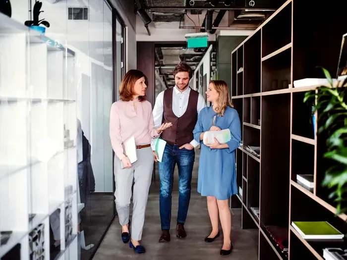 Three colleagues walk and talk in a modern office hallway, showing networking and services on City Directory Works